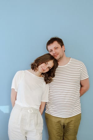 Woman resting her head on a mans shoulder, in front of a blue wall