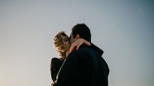 Man and woman in an emotional embrace with the sky in the background