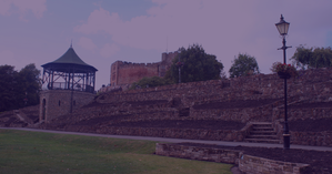 Tamworth Castle overlooking a grassy park, with layered stone walls, steps, and a historic tower under a cloudy sky.
