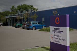 Exterior of Care Fertility Bath, a modern blue building with cars parked outside and a purple Care Fertility sign pointing to reception.