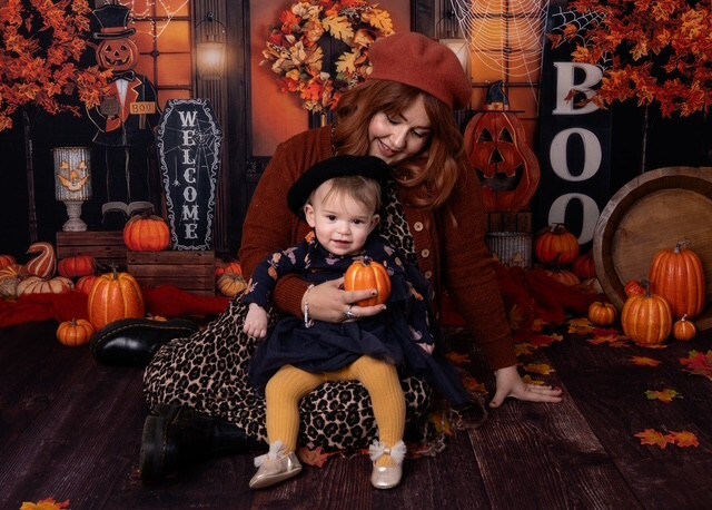 Becki and Betsy at a Halloween-themed pumpkin patch photo set, Betsy holding a small pumpkin