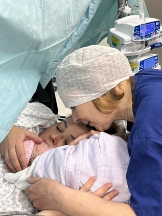 Becki holding newborn Betsy skin to skin in theatre just after her caesarean, with her mum smiling beside them