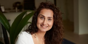 Curly-haired woman smiling, plant in background