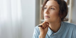 Woman by a window, chin on hand, looking thoughtful
