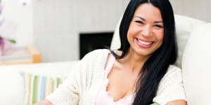 Dark-haired woman laughing on a sofa