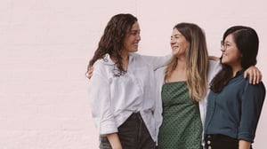 Three women smiling with their arms around each other, showing friendship and support during a fertility journey.