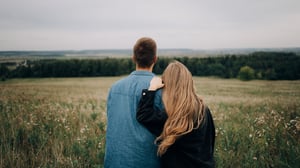 A couple standing together in a field, looking out across the countryside, representing future fertility planning and life timelines.