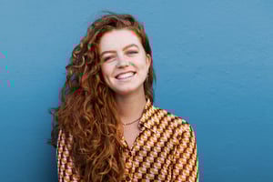 Smiling woman with long curly red hair standing against a blue background