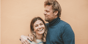 Man with arm around woman in front of a pale peach background