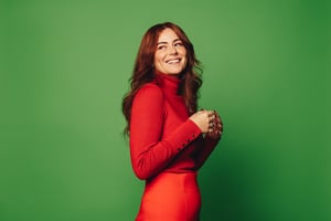 Red headed woman wearing a red high neck jumper and a matching red skirt against a green background