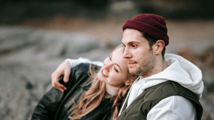 Blonde woman resting her head on male partners shoulder whilst he embraces her