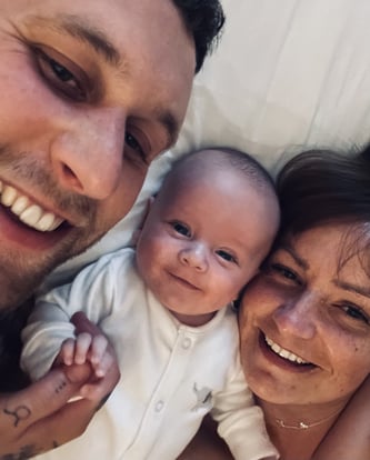 Alicia and Scott lying down with their baby son Frankie between them, smiling at the camera.