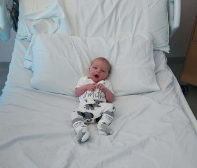 Newborn baby Zachary Brian Smith lying on a hospital bed, dressed in a white outfit shortly after birth.