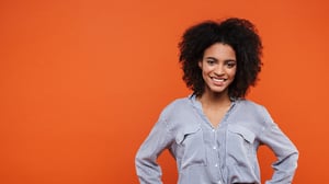 Smiling woman standing against an orange background, with her hands on her hips.
