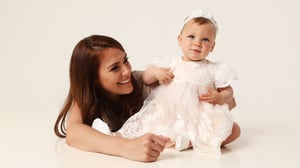 Melissa smiling at her baby daughter Sasha during a studio photo shoot, with Sasha wearing a pale dress.